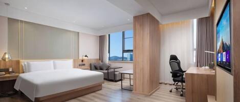 Una habitación de hotel moderna con una cama grande, un escritorio, una silla, un televisor y una ventana con vistas a la ciudad.