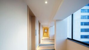 Un pasillo moderno de hotel con suelo de madera, paredes blancas y grandes ventanales a un lado.