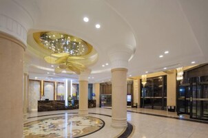 Un vestíbulo de hotel con una imponente lámpara de araña, columnas de mármol y una recepción.