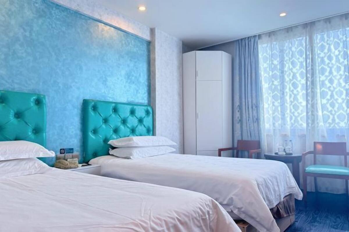 A hotel room with two beds, a large window with patterned curtains, and a wardrobe.
