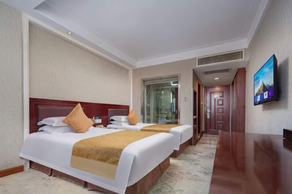 A hotel room with two beds, a TV, and a glass door leading to a bathroom.