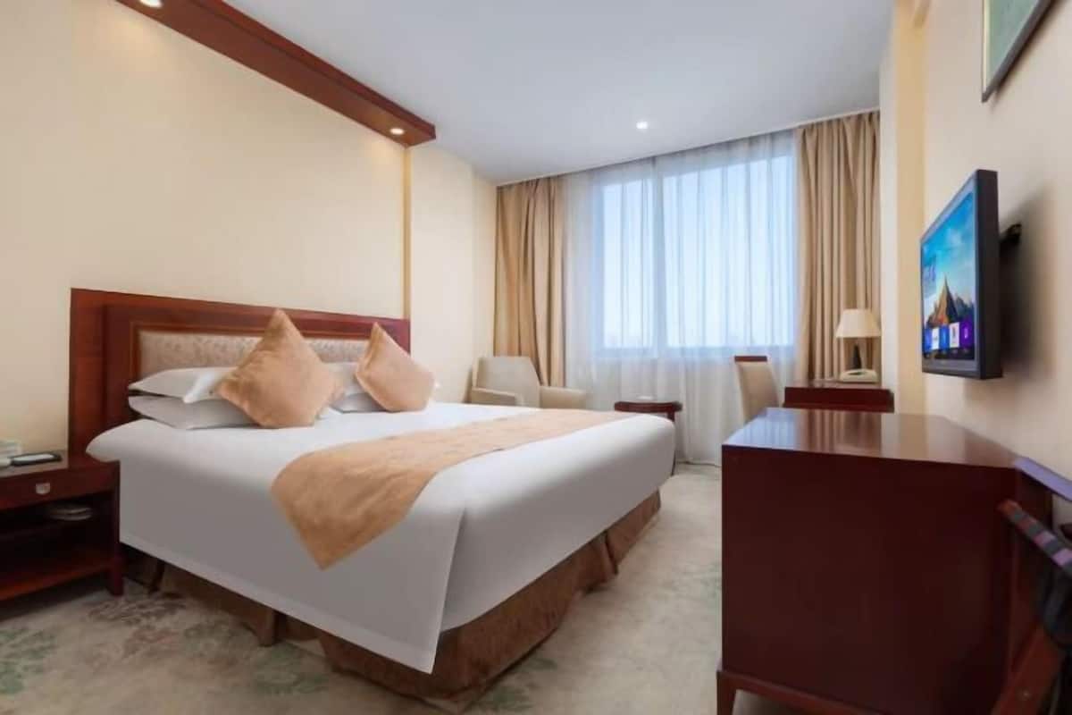 A hotel room with a bed, bedside table, chair, desk, and a television.
