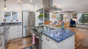 Una cocina moderna con un refrigerador de acero inoxidable, un horno y una estufa integrada. Hay una isla grande con encimera de mármol y un florero.