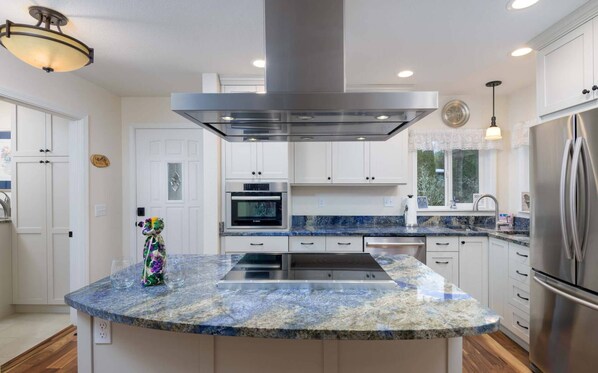Kitchen features a central island with stovetop and range hood, stainless steel appliances, and granite countertops.