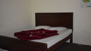 Uma cama de solteiro com cabeceira de madeira, roupa de cama branca e um cobertor vermelho.
