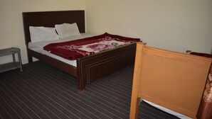 Uma cama de solteiro com cabeceira de madeira, um cobertor com padrão vermelho e branco e uma pequena mesa de cabeceira.