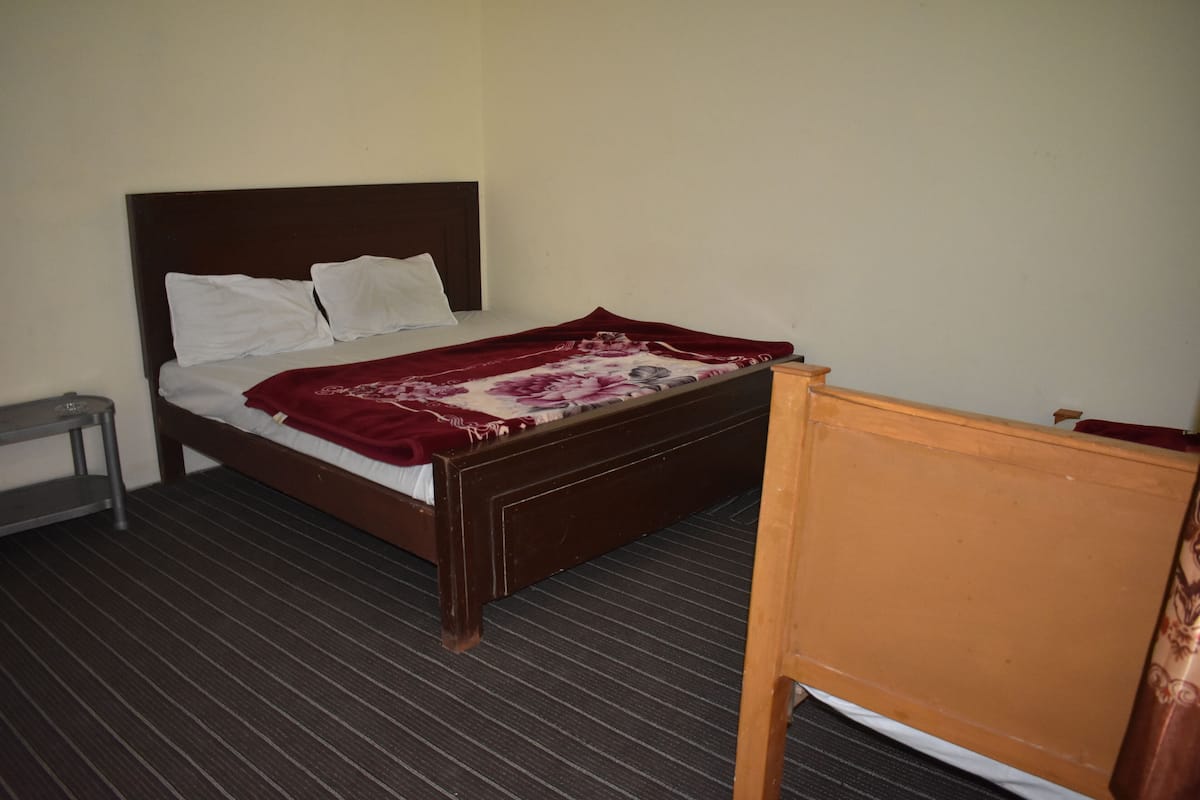 A single bed with a wooden headboard, a red and white patterned blanket, and a small bedside table.