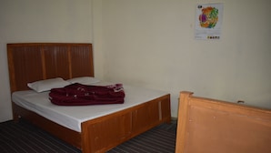 Uma cama de solteiro com cabeceira e peseira de madeira, colchão branco e um cobertor vermelho dobrado sobre a cama.