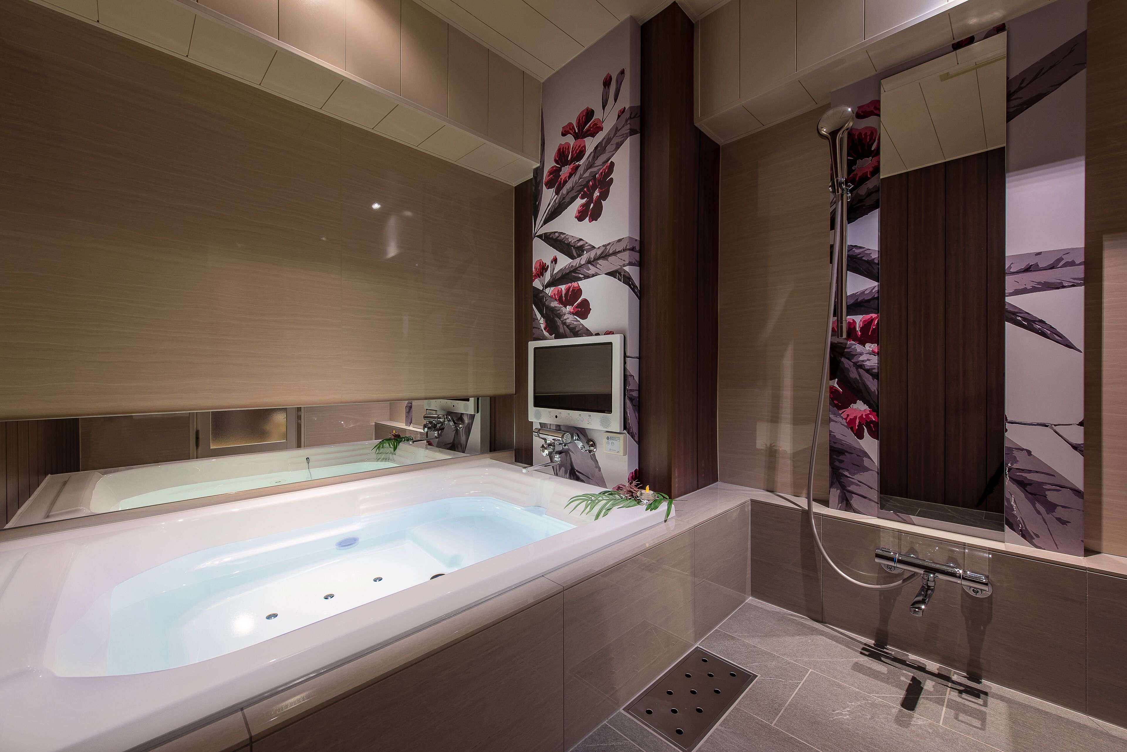 A modern bathroom with a large bathtub, a shower, and a mirror with floral wallpaper.