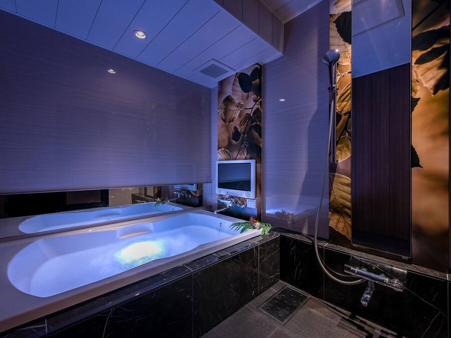 A modern bathroom with a large bathtub, a shower, and a wall-mounted TV.