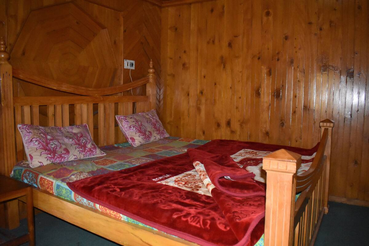 A wooden bed with a quilt and pillows, a wooden headboard, and a wooden wall.