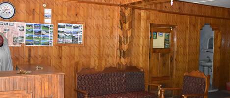 A wooden interior with a reception desk, patterned sofa, and wooden chairs.