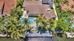 An aerial view of a residential property with a swimming pool, multiple buildings, and surrounding palm trees.