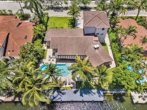 Vista aérea de una propiedad residencial con piscina, varias edificaciones y palmeras circundantes.