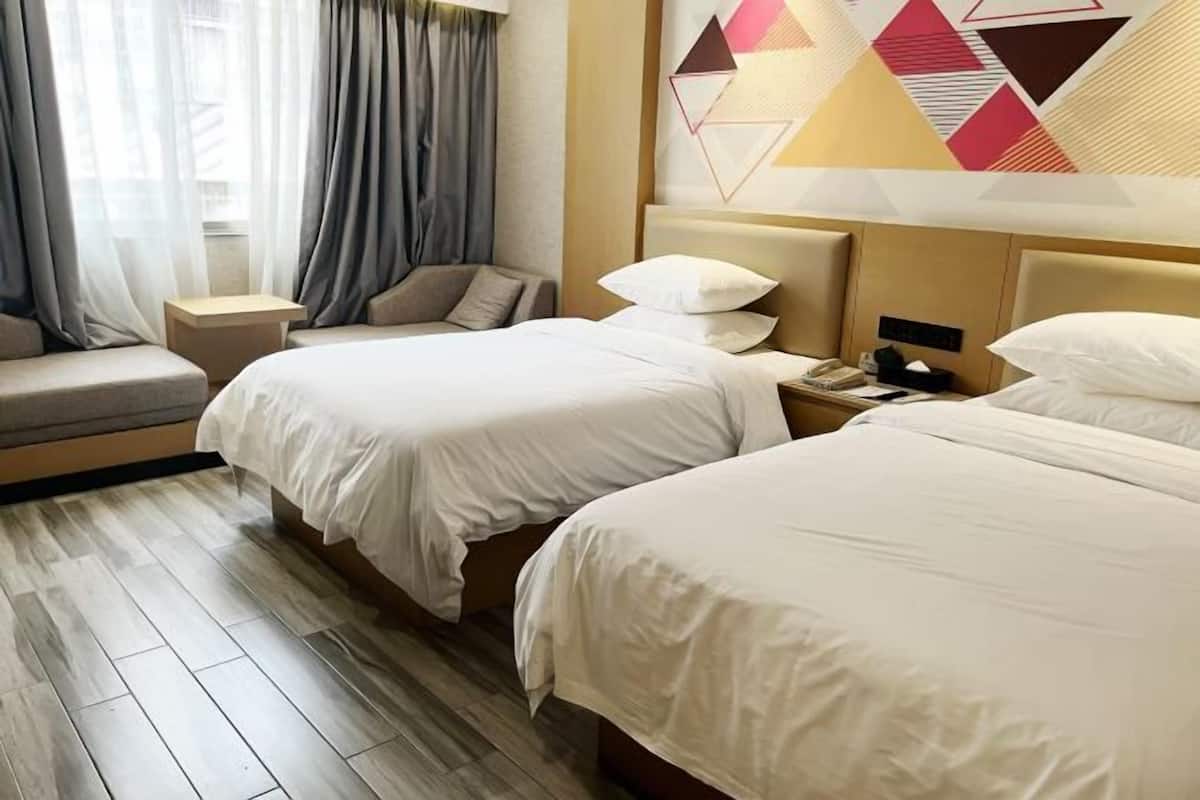 A hotel room with two beds, a bedside table, a lamp, and a geometric wall decoration.