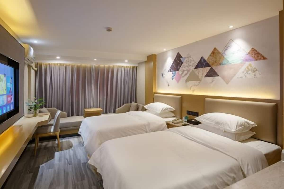 A hotel room with two beds, a desk with a TV, a wall art piece, and a large window with curtains.