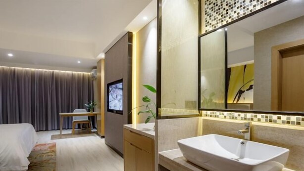 A modern hotel room with a bed, a desk, a television, a bathroom with a large mirror and a sink. - Jinhua Hot Spring Hotel (Luchuan)