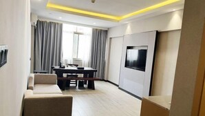 A modern living room with a sofa, a dining table, and a TV mounted on the wall. - Jinhua Hot Spring Hotel (Luchuan)