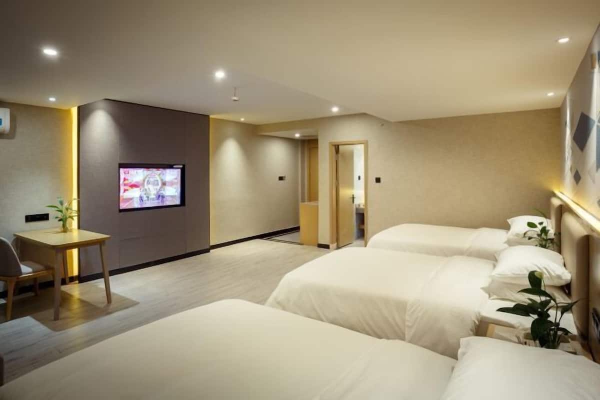 A hotel room with three beds, a TV, a desk, and a small table with a plant.