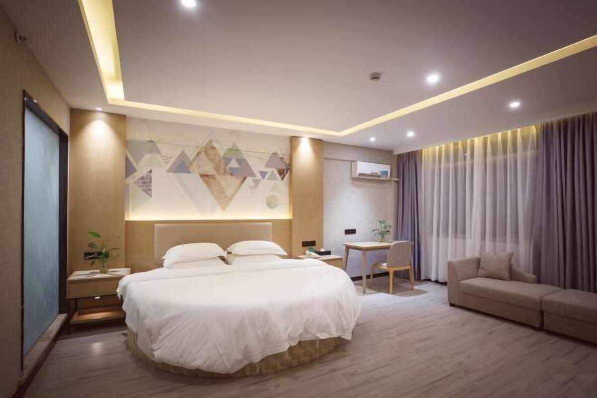 A modern hotel room with a large bed, a desk, a sofa, and a wall with geometric patterns.