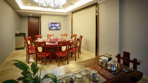 A dining area with a round table, red chairs, a chandelier, a television, and a small kitchenette. - Jinhua Hot Spring Hotel (Luchuan)