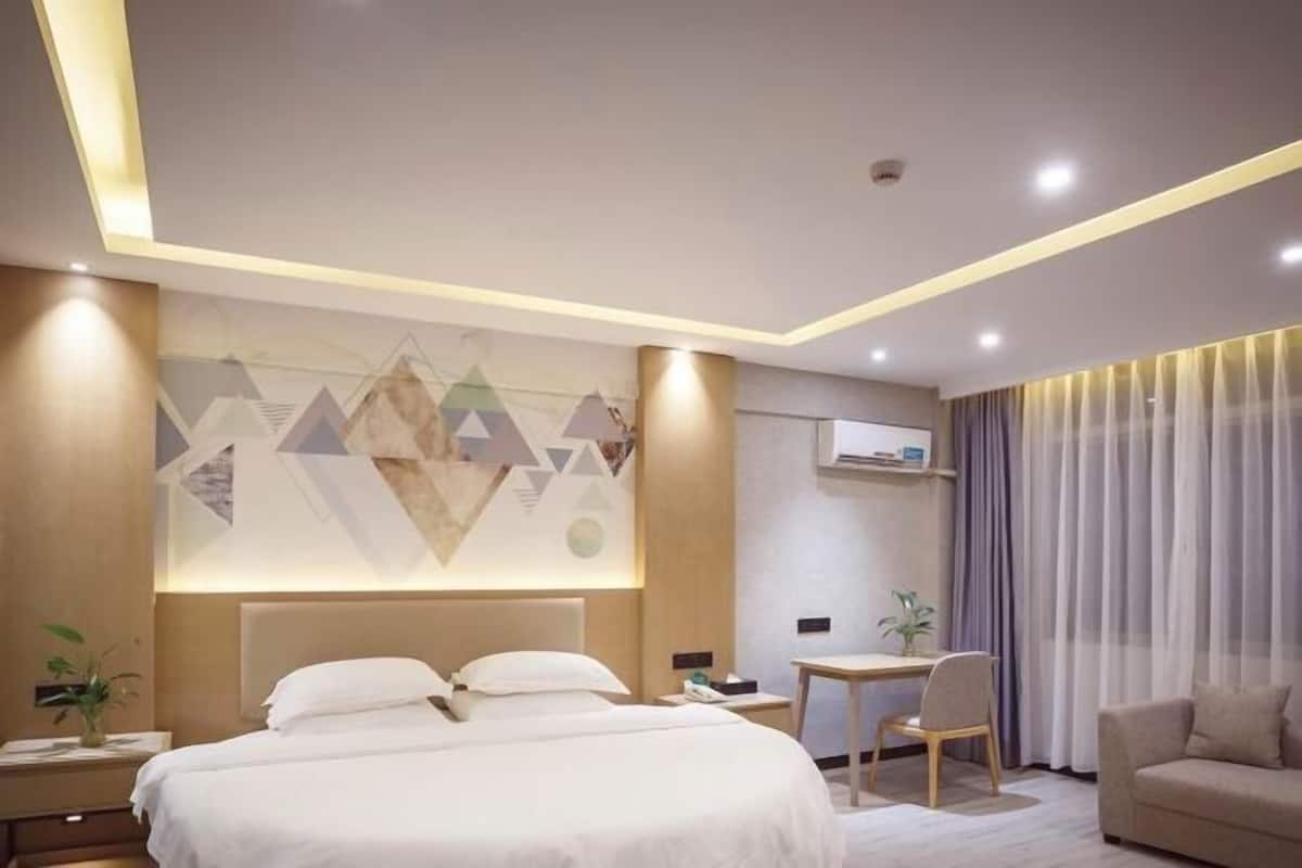A modern hotel room with a large bed, a desk, a chair, and a sofa.
