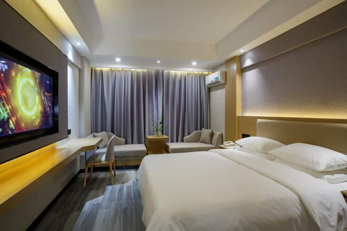 A hotel room with a large flat-screen TV, two beds, a desk, and a chair.
