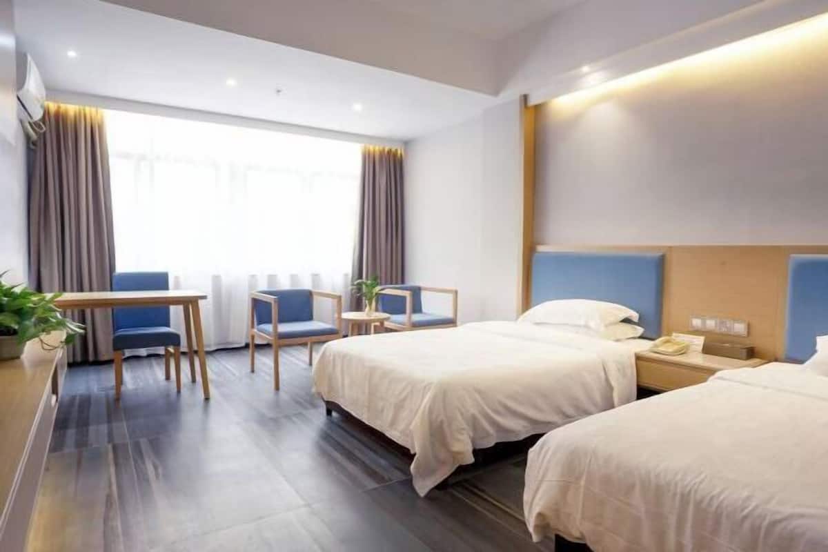 A hotel room with two beds, a desk, a chair, a small table, and a window with curtains.