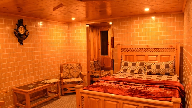 A wooden-paneled room with a bed, a chair, and a small table. - The Kylix (Balakot)
