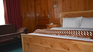 A wooden-paneled room with a bed, a nightstand, a striped chair, and a wooden door. - The Kylix (Balakot)
