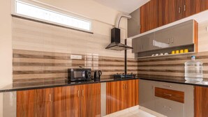 A modern kitchen with wooden cabinets, a black countertop, a built-in microwave, a coffee maker, and a water dispenser. - Pinnacle Serviced Apartments (Bengaluru)
