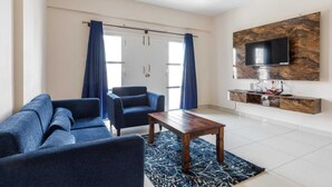 A modern living room with a sofa, armchairs, a coffee table, and a TV mounted on a stone wall. - Pinnacle Serviced Apartments (Bengaluru)