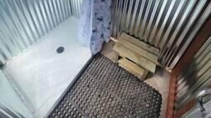 Een kamer met een metalen frame, een douchegedeelte, een klein houten bankje en een metalen rooster.
