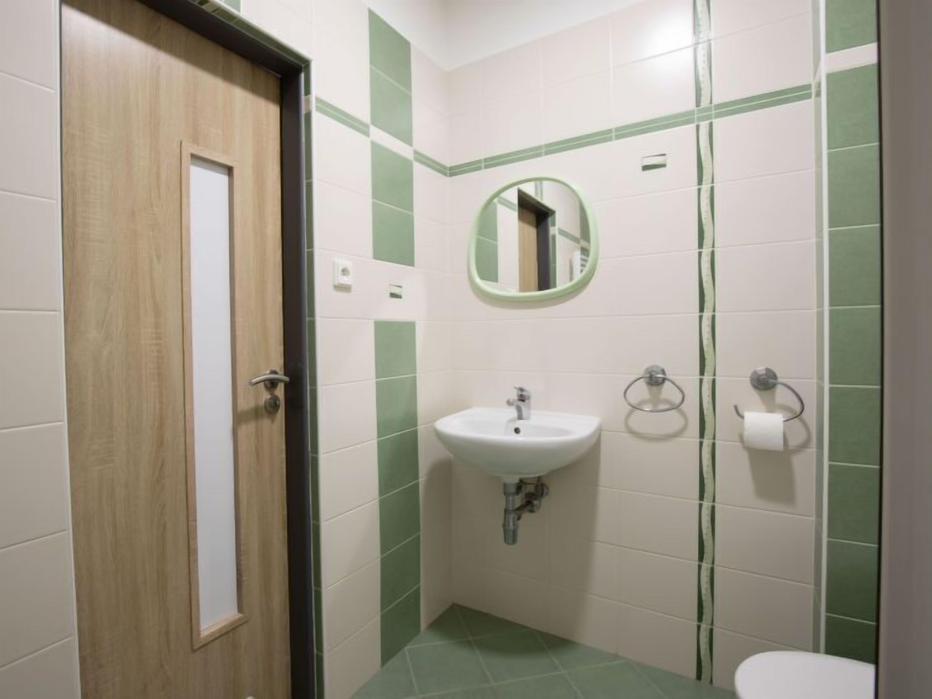 A small bathroom with a wooden door, a sink with a mirror, and a toilet.