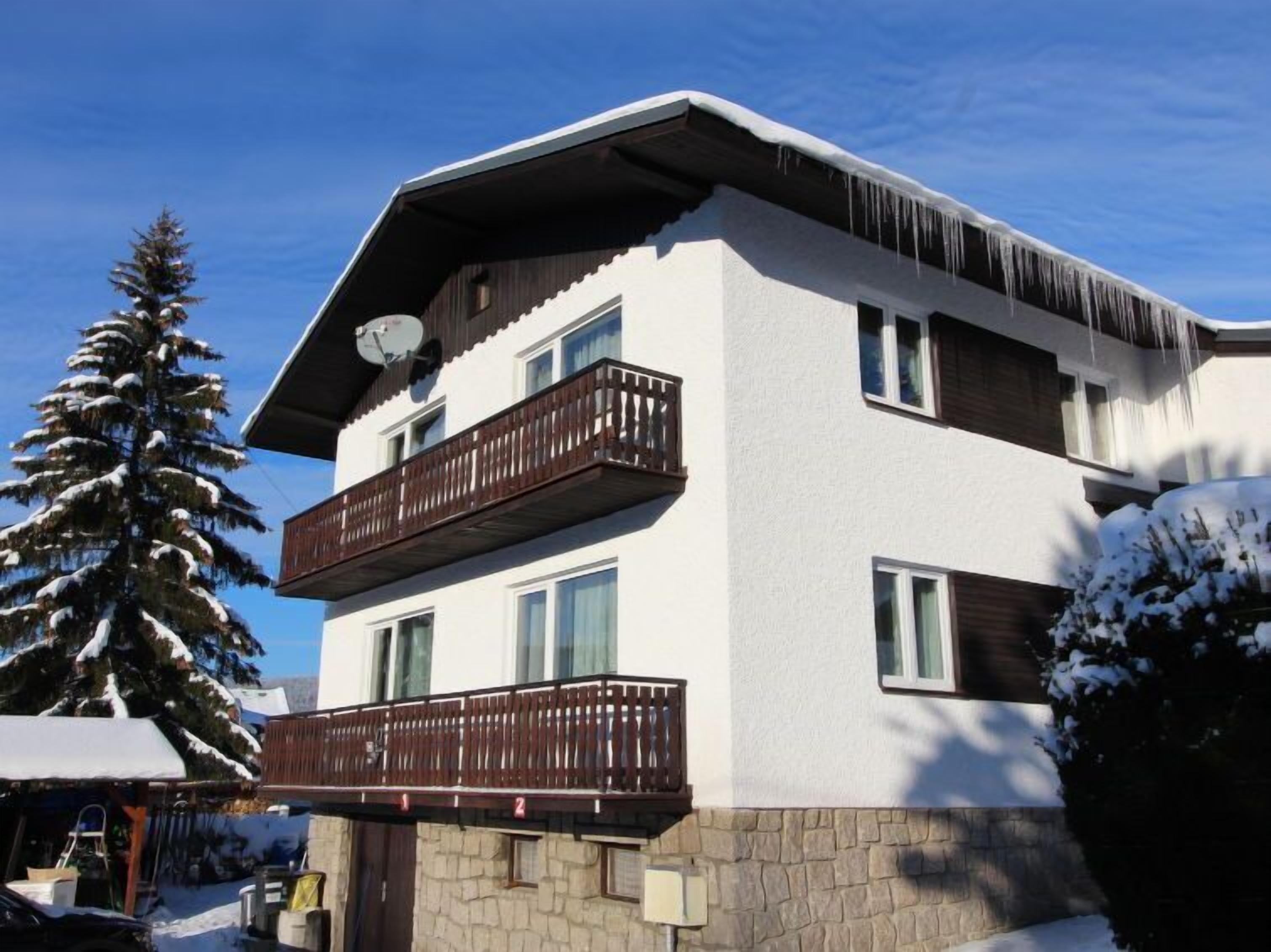 Un immeuble à plusieurs étages, doté de balcons et d’une base en pierre, se dressant sous un ciel d’un bleu limpide.