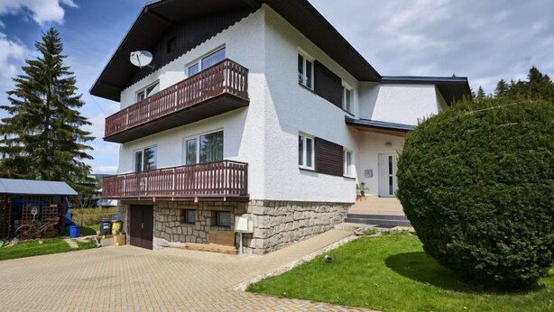 Ein zweistöckiges Gebäude mit Natursteinfassade, einem Holzbalkon und einem gepflasterten Auffahrt.
