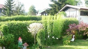 Ein gepflegter Garten mit Hecke, Vogelhaus und einer Personenstatue.