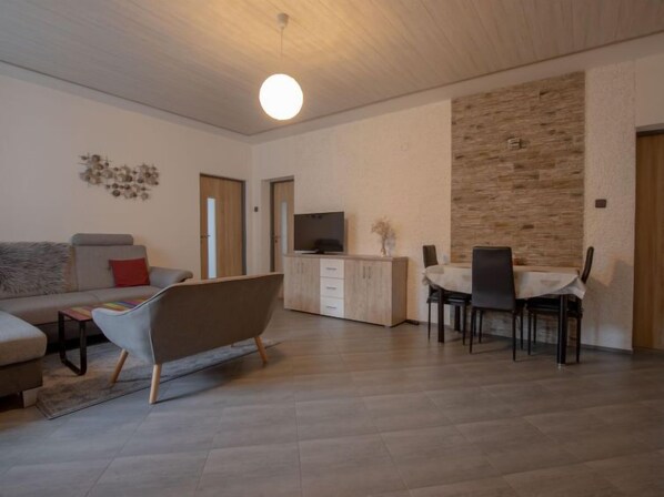 A modern living room with a sofa, a unique armchair, a dining area with a table and chairs, a TV on a wooden cabinet, and a stone accent wall. - Ski & Garden Nook by Interhome (Harrachov)