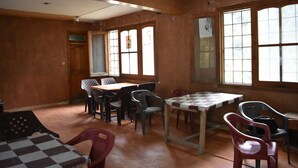 Una habitación con techo alto, paredes de madera y ventanas amplias. Varias mesas y sillas están dispuestas para comer.