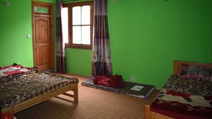 Una habitación con dos camas, una puerta de madera, una ventana con cortinas y una pared verde.