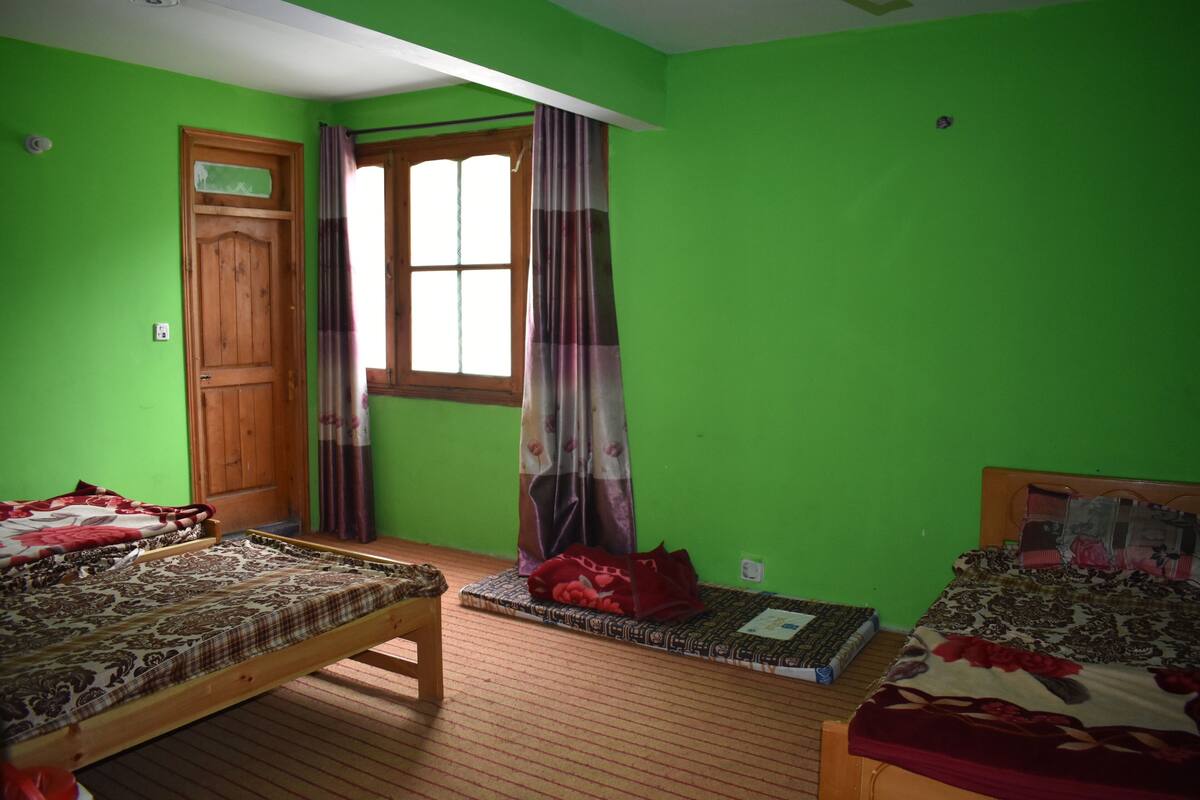 A room with two beds, a wooden door, a window with curtains, and a green wall.