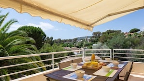 A balcony with a table set for breakfast, surrounded by a white railing, overlooking a lush landscape with trees and houses. - Les Mas de la Mer by Interhome (Saint Aygulf)