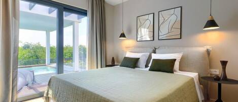 A spacious bedroom with a large bed, a view of a swimming pool, and two abstract art pieces on the wall.