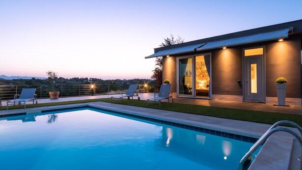 A modern poolside area with a clear view of the pool, lounge chairs, and a building with large windows and a door. - Villa Atmosfere 8 in Frassi (Arce)