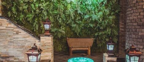 Un espacio interior acogedor con una pared de musgo, un banco de madera y faroles en el suelo.