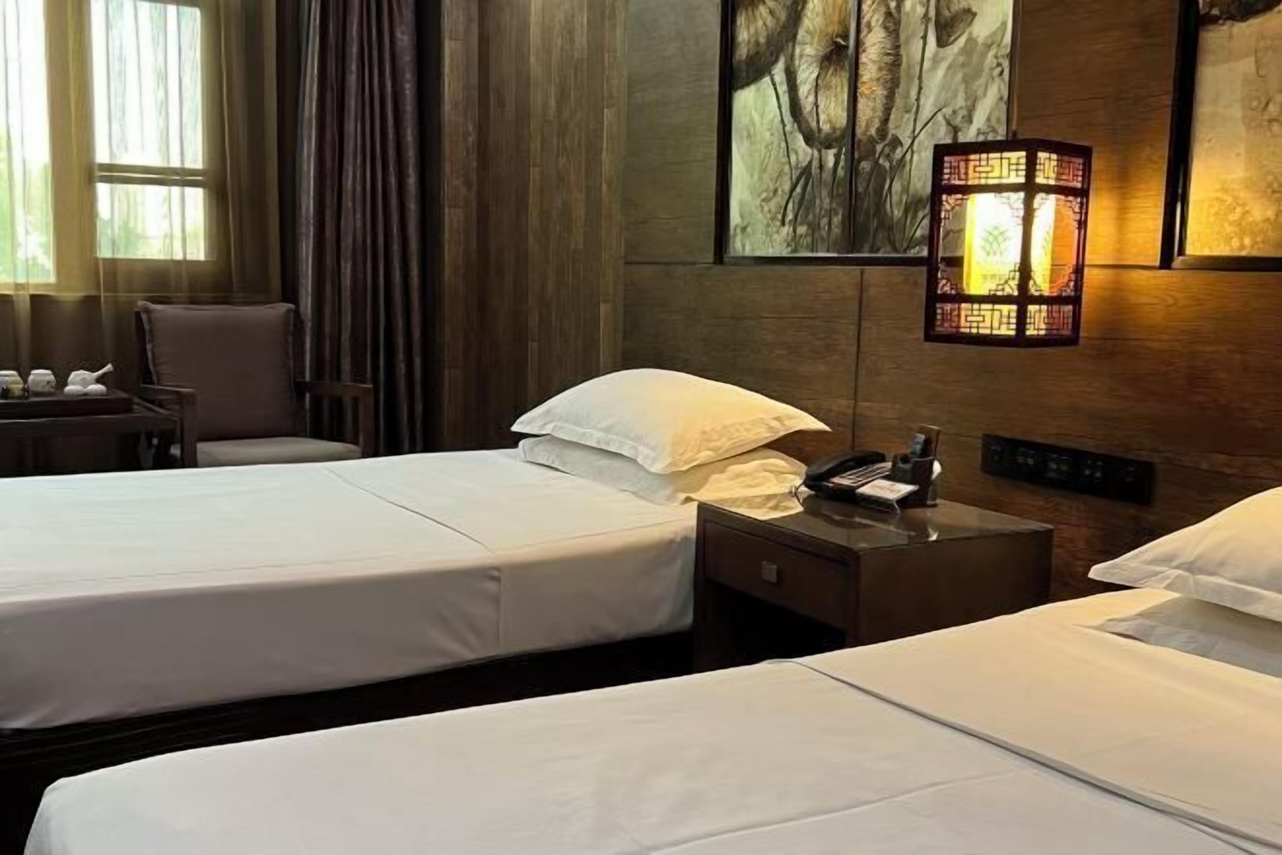 Habitació d'hotel amb dos llits, una cadira, una taula de nit amb un telèfon i una làmpada penjada a la paret.