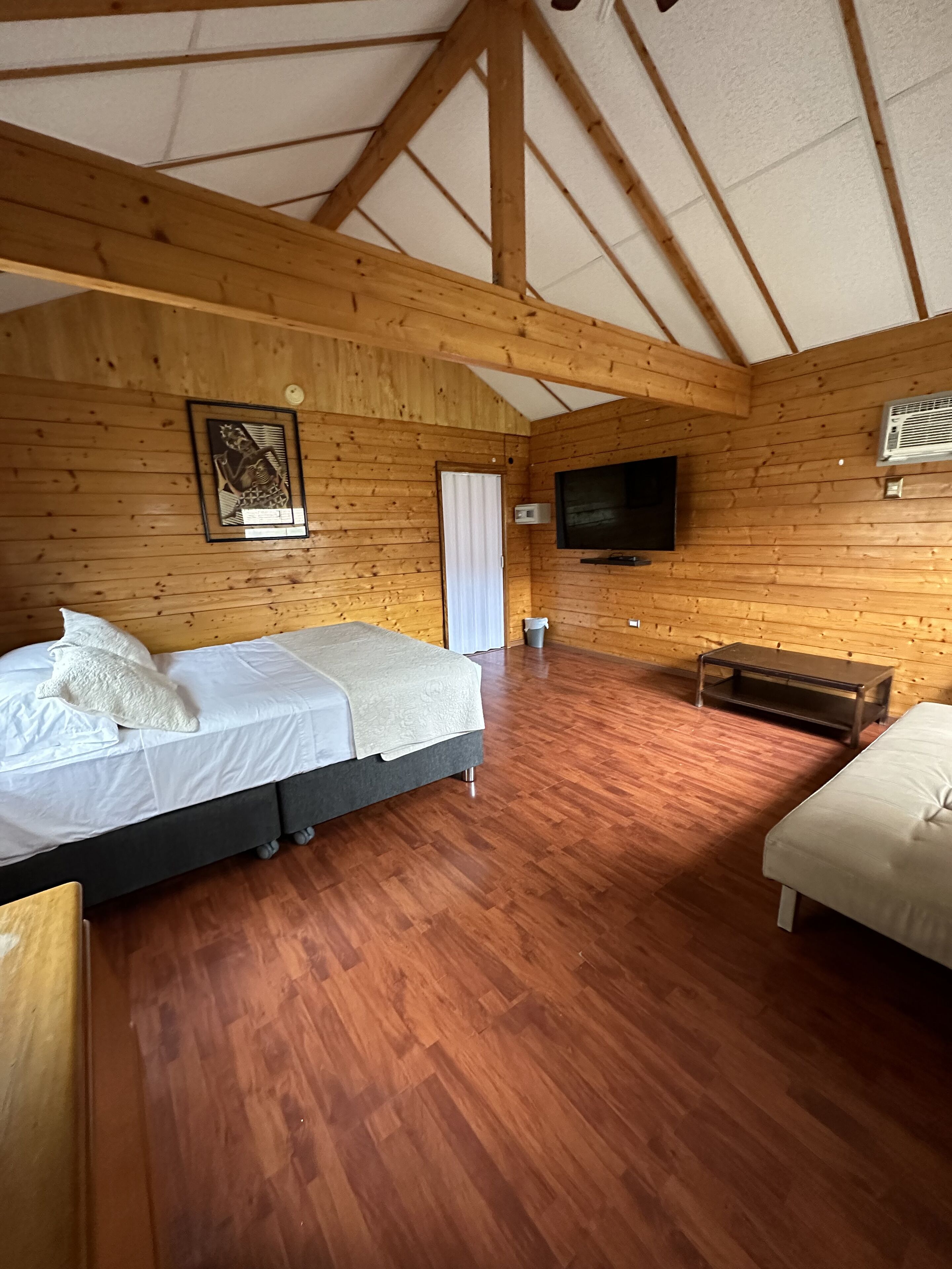Een kamer met houten lambrisering, een bed, een bankje en een televisie.