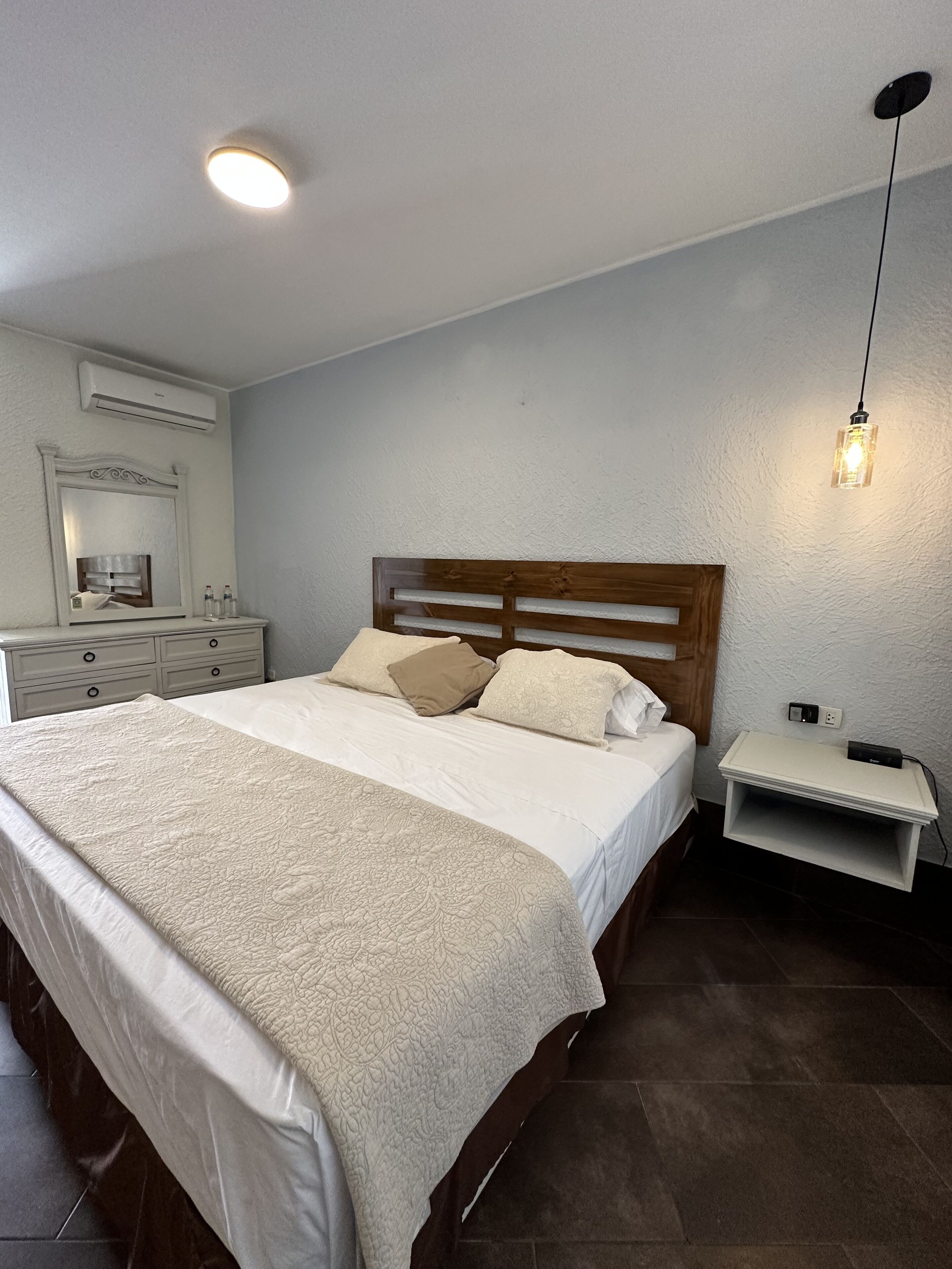 A bedroom with a large bed, a nightstand, a mirror, and a ceiling light.