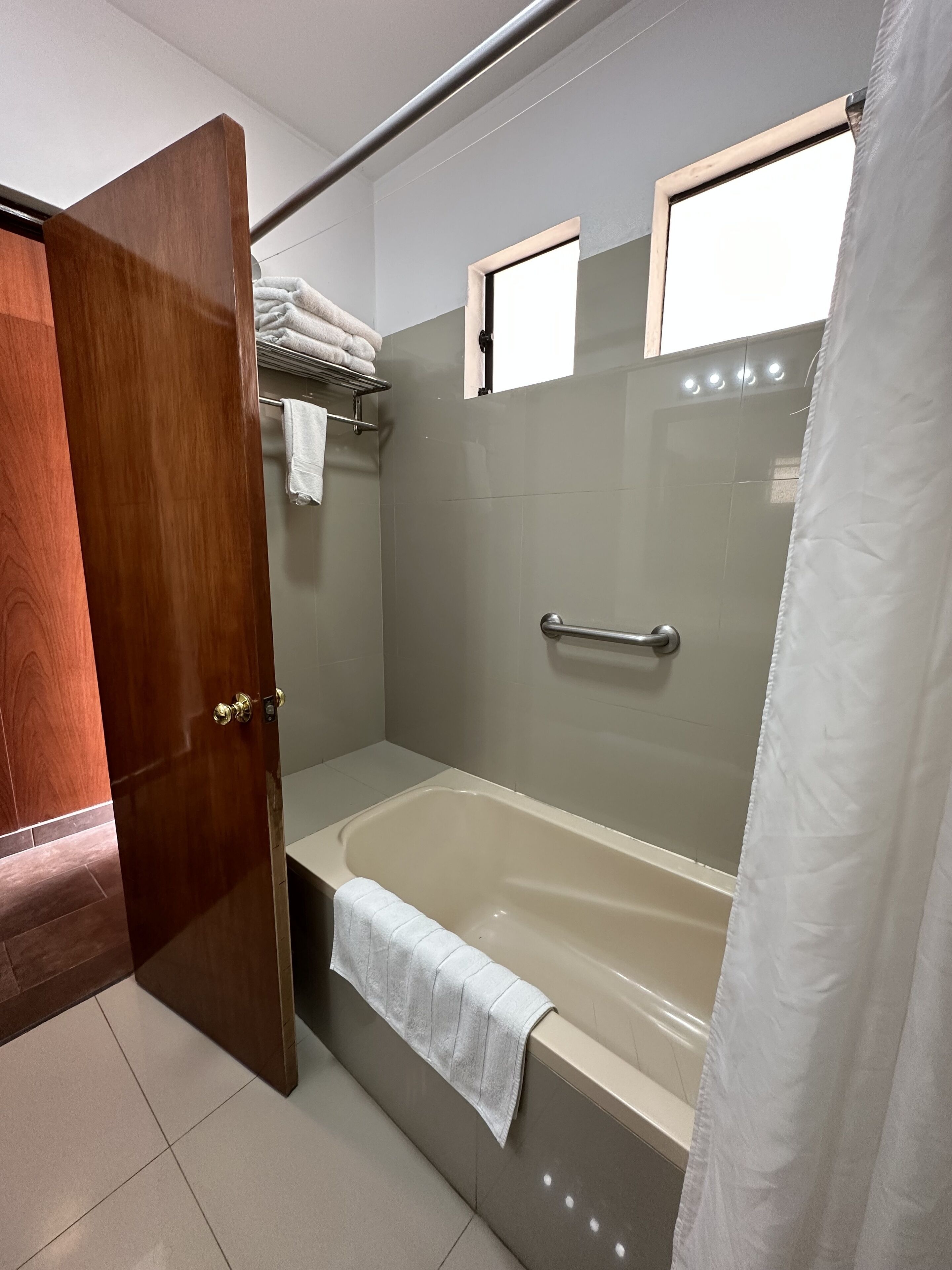 A modern bathroom with a wooden door, a bathtub, a shower area, and a towel rack.