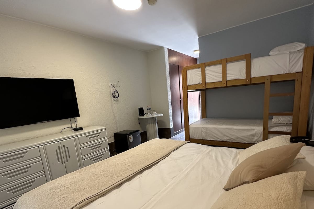 Un dormitorio con una cama grande, televisión, escritorio y literas.